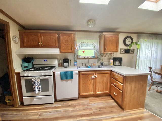 kitchen with white appliances, a peninsula, light countertops, under cabinet range hood, and a sink