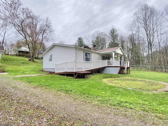 back of house featuring a deck, a chimney, fence, and a lawn