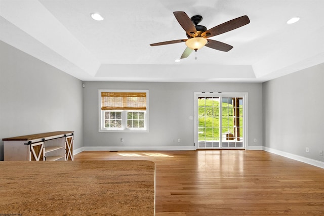 unfurnished room with a tray ceiling, light wood finished floors, baseboards, and recessed lighting