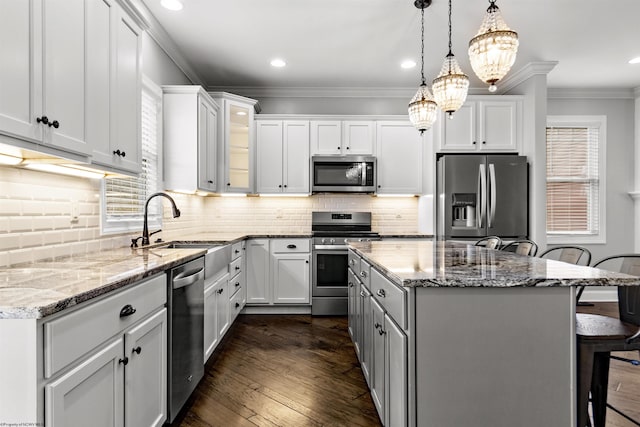 kitchen with ornamental molding, a kitchen island, a kitchen bar, stainless steel appliances, and pendant lighting