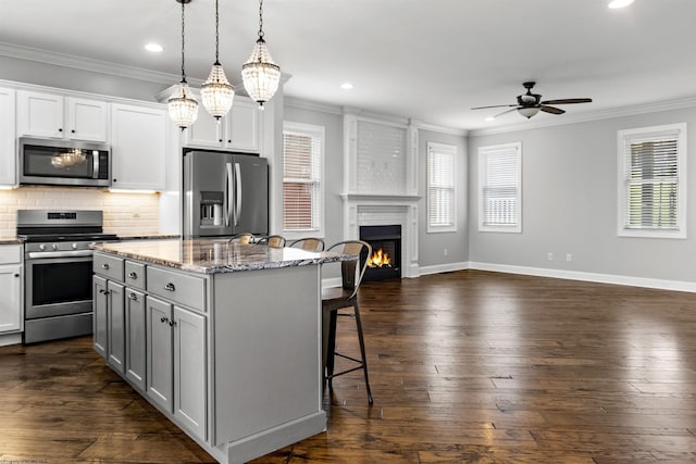 kitchen with a kitchen breakfast bar, open floor plan, a ceiling fan, crown molding, and appliances with stainless steel finishes