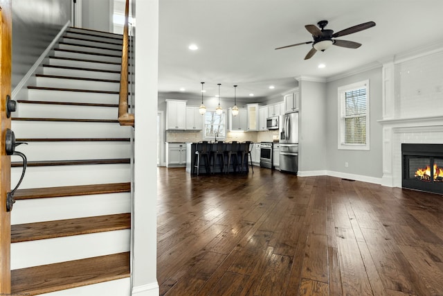 living area with crown molding, ceiling fan, a wealth of natural light, and stairs