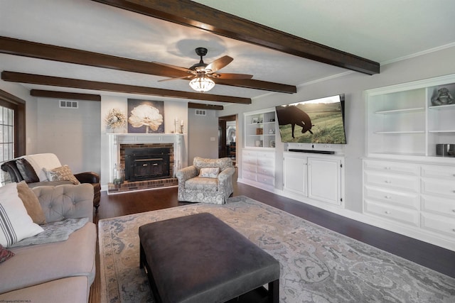 living area featuring dark wood-style flooring, visible vents, a fireplace with raised hearth, beamed ceiling, and ceiling fan