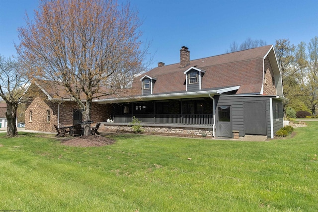 rear view of property with a lawn, a gambrel roof, a chimney, and a shingled roof