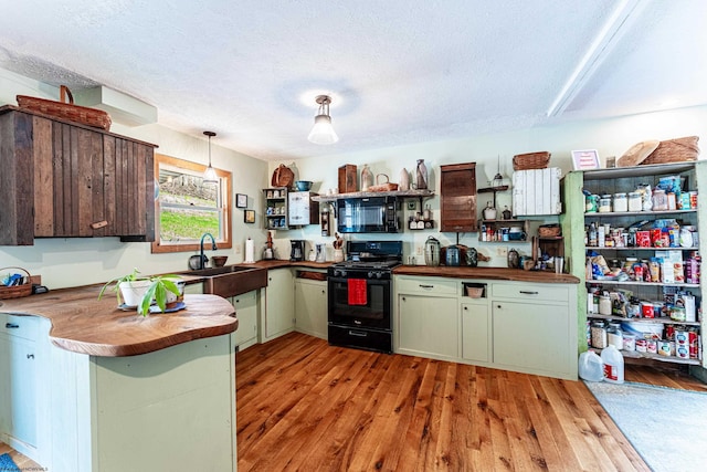 kitchen with open shelves, a sink, light wood-style floors, black appliances, and butcher block countertops