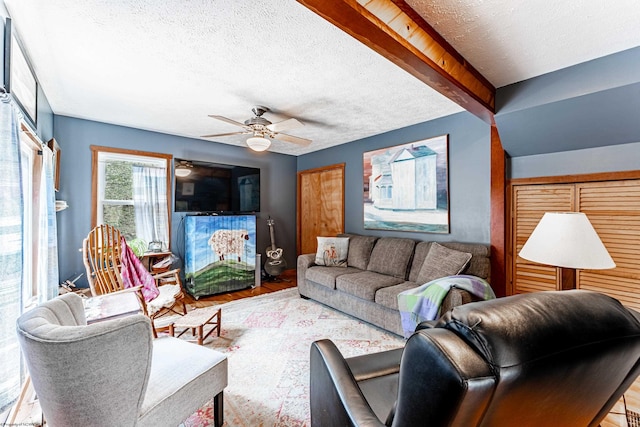 living area with beamed ceiling, a ceiling fan, wood finished floors, and a textured ceiling