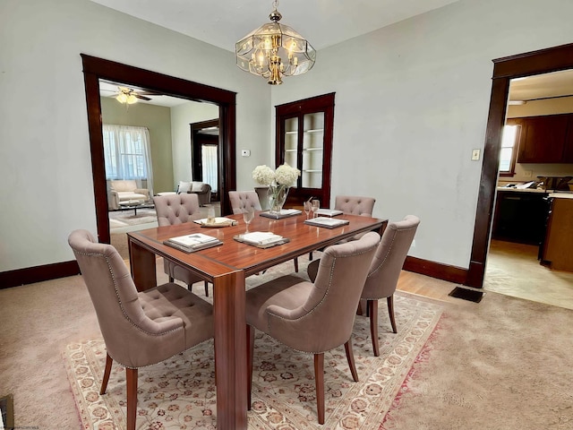 dining area featuring light carpet, a healthy amount of sunlight, ceiling fan with notable chandelier, and baseboards