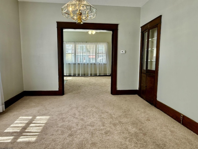 carpeted spare room featuring baseboards and a notable chandelier