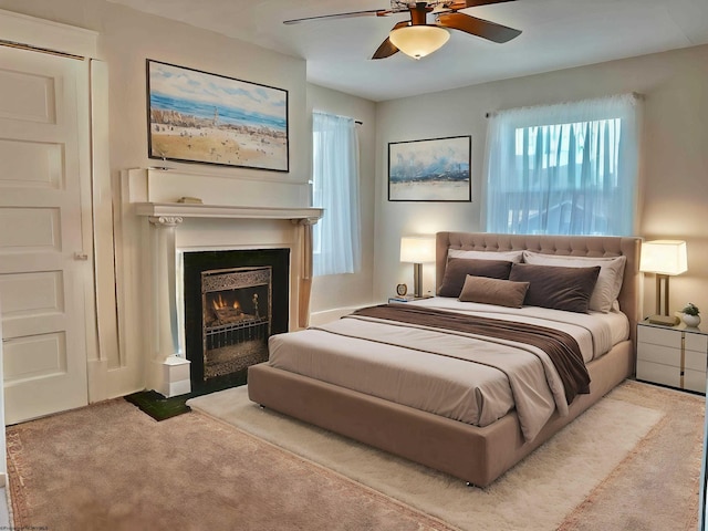 bedroom featuring a fireplace with flush hearth, a ceiling fan, carpet flooring, and multiple windows