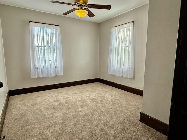 carpeted empty room with plenty of natural light, a ceiling fan, and baseboards
