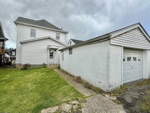 view of side of home with a lawn, a detached garage, entry steps, and concrete block siding