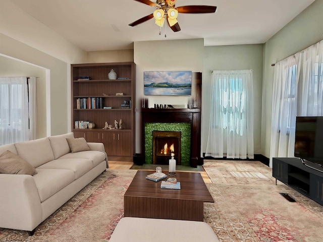 living area featuring a tiled fireplace, a ceiling fan, visible vents, and a healthy amount of sunlight