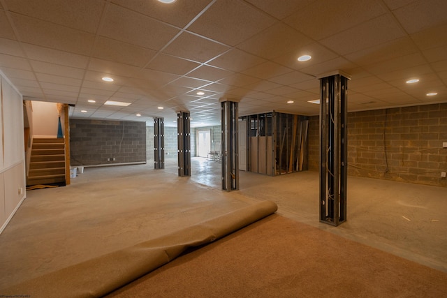 below grade area with concrete block wall, a paneled ceiling, carpet, and stairway