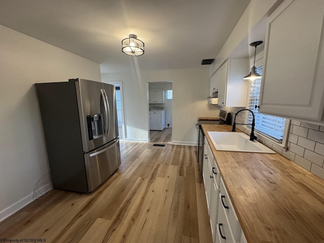kitchen with a sink, decorative backsplash, butcher block counters, appliances with stainless steel finishes, and washer / clothes dryer