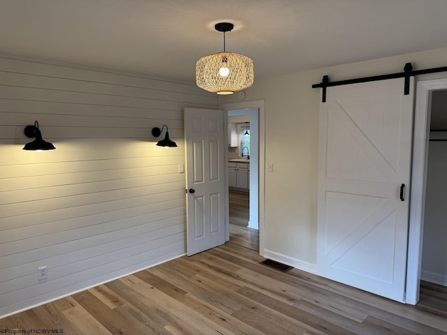 unfurnished dining area featuring a barn door, wood finished floors, visible vents, and a sink