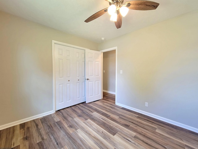 unfurnished bedroom with wood finished floors, a closet, a ceiling fan, and baseboards