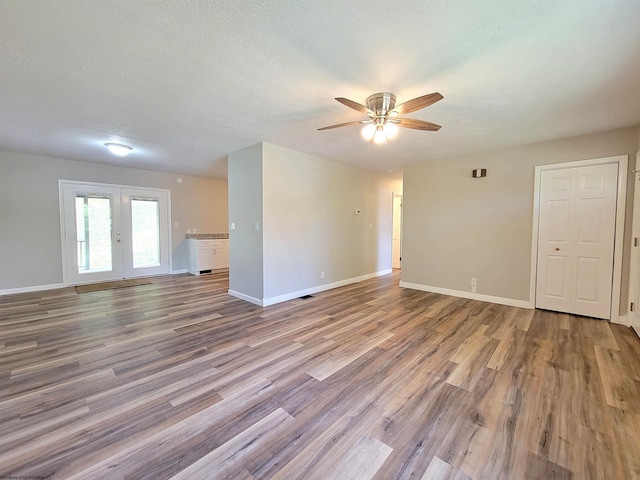 unfurnished room with wood finished floors, a ceiling fan, french doors, baseboards, and a textured ceiling