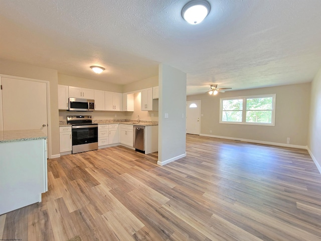 kitchen featuring light wood finished floors, open floor plan, baseboards, ceiling fan, and appliances with stainless steel finishes