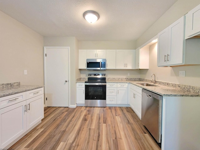 kitchen with light wood finished floors, a sink, white cabinetry, light stone countertops, and appliances with stainless steel finishes