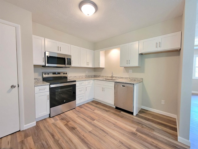 kitchen featuring stainless steel appliances, a sink, light wood-type flooring, light stone countertops, and white cabinetry