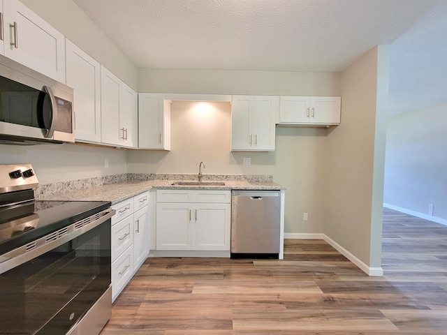 kitchen with light stone counters, a sink, light wood-type flooring, white cabinets, and appliances with stainless steel finishes