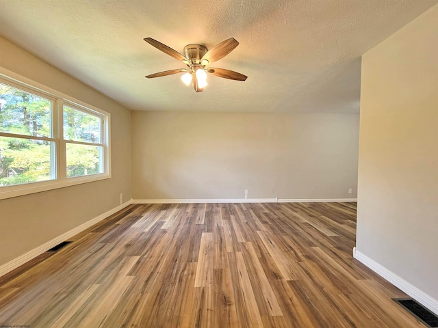spare room with wood finished floors, visible vents, a ceiling fan, and baseboards