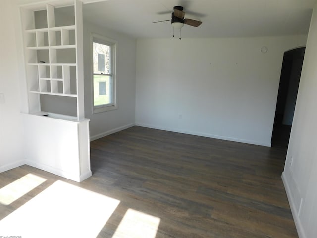 unfurnished room featuring dark wood-type flooring, arched walkways, baseboards, and ceiling fan