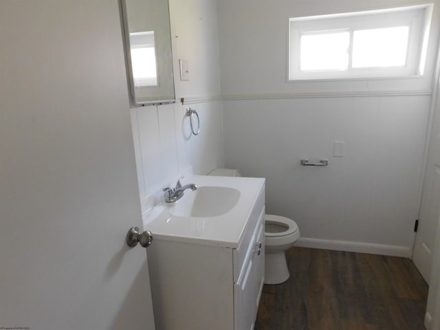 half bath with wainscoting, toilet, vanity, and wood finished floors