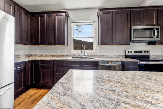kitchen with a sink, light wood-type flooring, dark brown cabinetry, light stone countertops, and appliances with stainless steel finishes