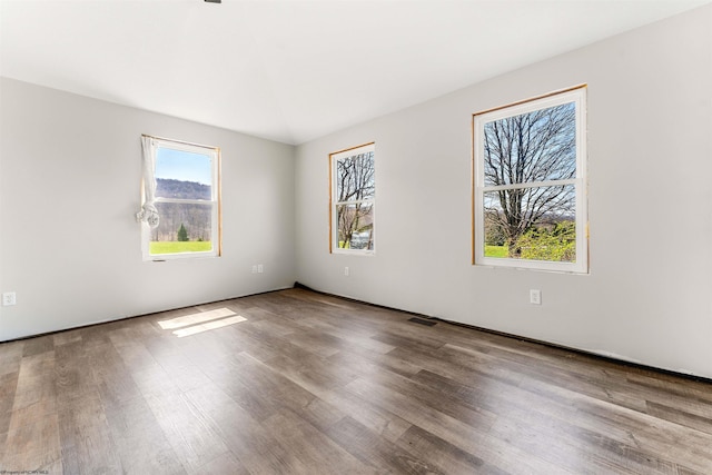 spare room with wood finished floors, visible vents, and a healthy amount of sunlight
