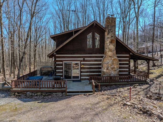 view of front facade featuring a wooden deck, a chimney, and log siding