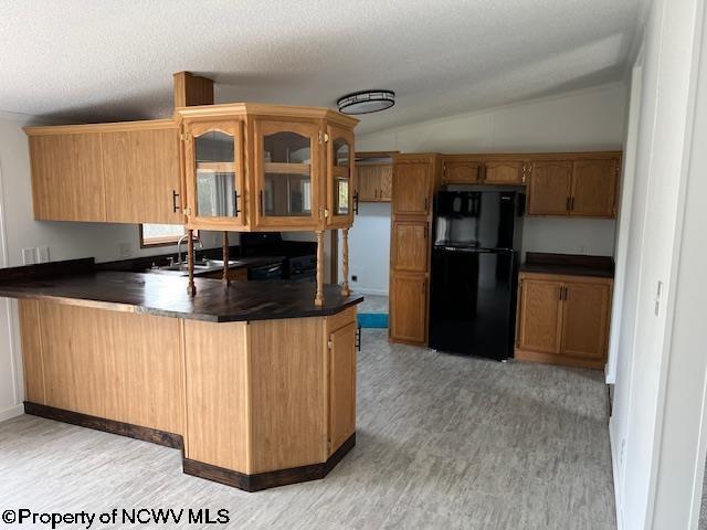 kitchen with dark countertops, a peninsula, freestanding refrigerator, and glass insert cabinets