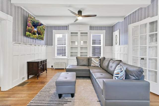 living area featuring a ceiling fan, wood finished floors, wallpapered walls, wainscoting, and radiator