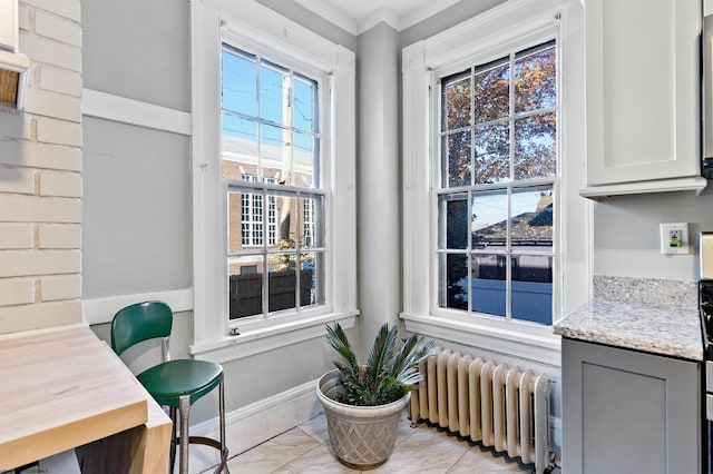 living area with radiator, plenty of natural light, marble finish floor, and ornamental molding
