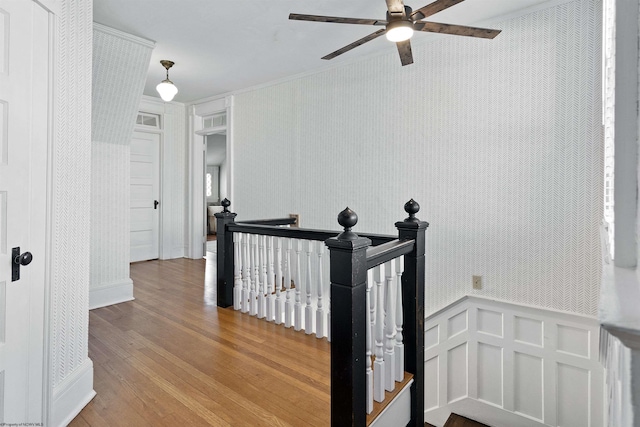 hall featuring wallpapered walls, wood finished floors, ornamental molding, and an upstairs landing