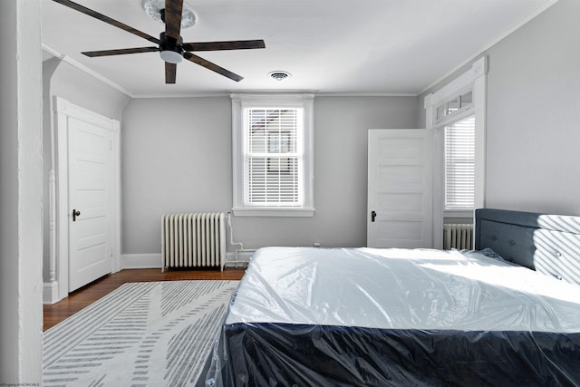 bedroom with radiator heating unit, wood finished floors, visible vents, crown molding, and baseboards