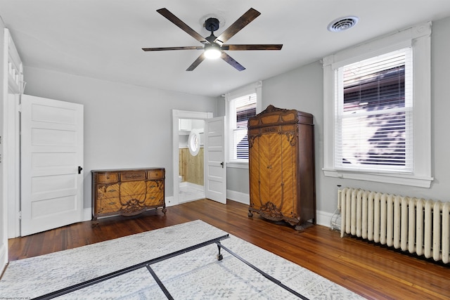 bedroom featuring radiator heating unit, wood finished floors, ensuite bath, baseboards, and ceiling fan
