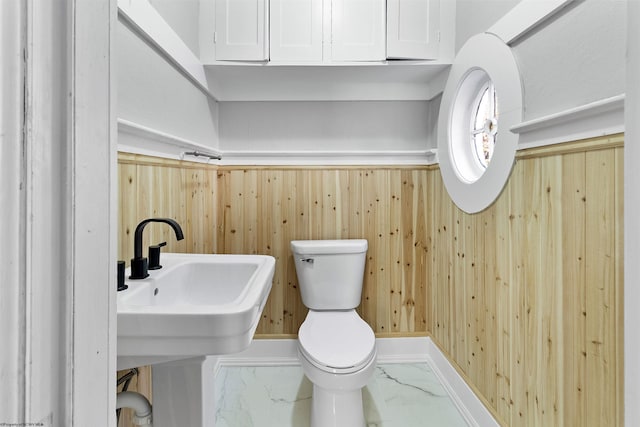bathroom with wood walls, marble finish floor, a sink, and toilet