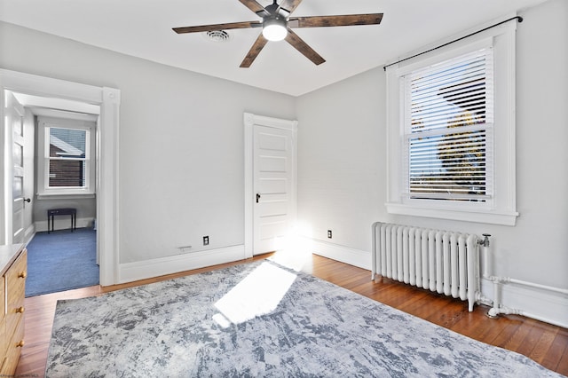 unfurnished bedroom featuring radiator heating unit, visible vents, ceiling fan, and wood finished floors