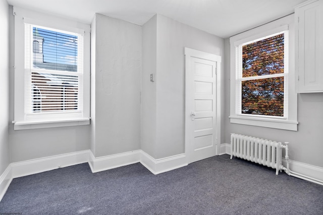empty room featuring plenty of natural light, baseboards, dark carpet, and radiator