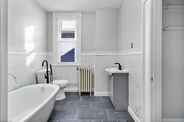 bathroom with radiator, a wainscoted wall, toilet, tile walls, and a freestanding tub