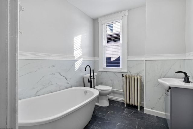 full bathroom featuring radiator, vanity, tile walls, wainscoting, and a soaking tub