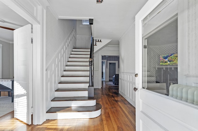 stairway featuring crown molding, wainscoting, wallpapered walls, a decorative wall, and wood-type flooring