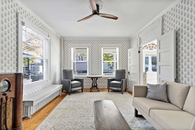 living area featuring a ceiling fan, crown molding, wood finished floors, and wallpapered walls