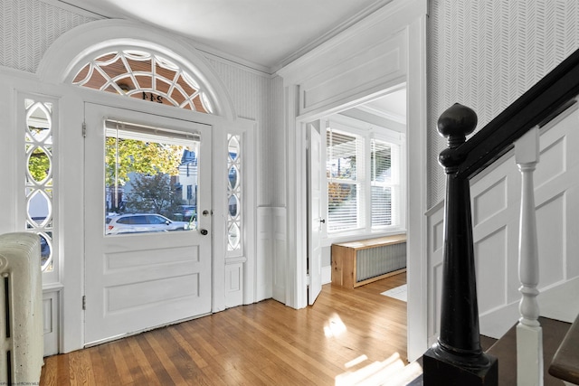 foyer with wallpapered walls, a wealth of natural light, light wood-style floors, and crown molding