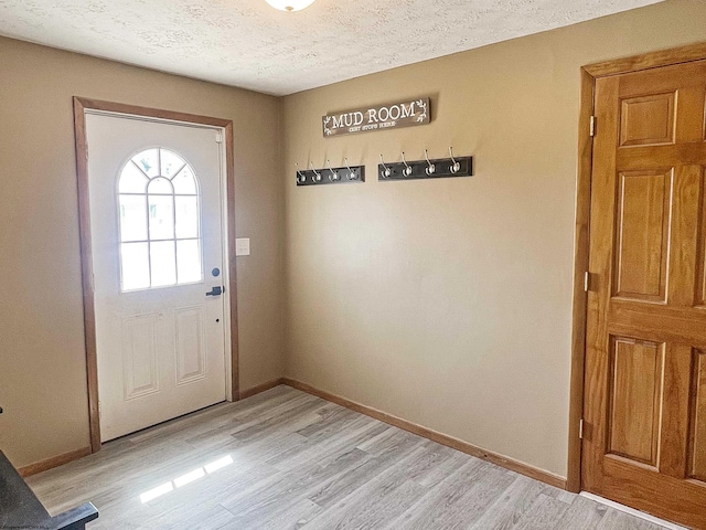 doorway featuring light wood-style floors, a textured ceiling, and baseboards