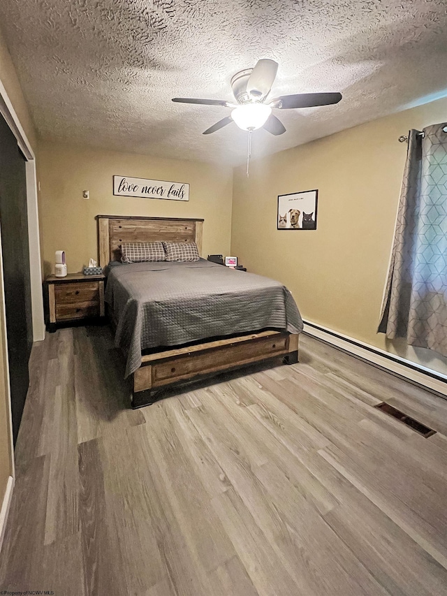 bedroom featuring a ceiling fan, wood finished floors, a textured ceiling, and baseboard heating