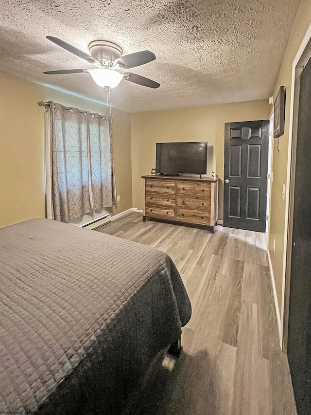 bedroom with wood finished floors, a ceiling fan, a baseboard heating unit, baseboards, and a textured ceiling