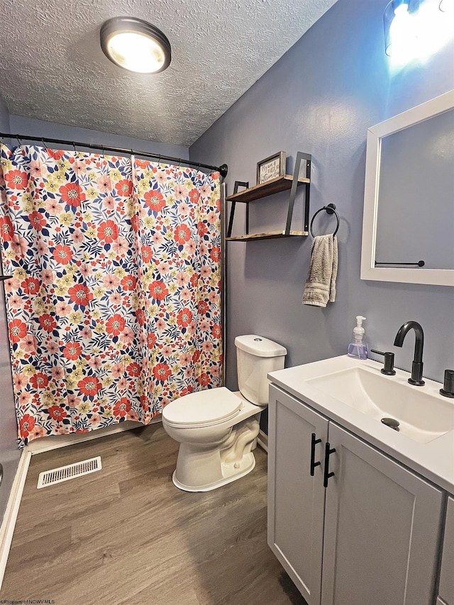 full bathroom featuring a textured ceiling, toilet, visible vents, wood finished floors, and vanity