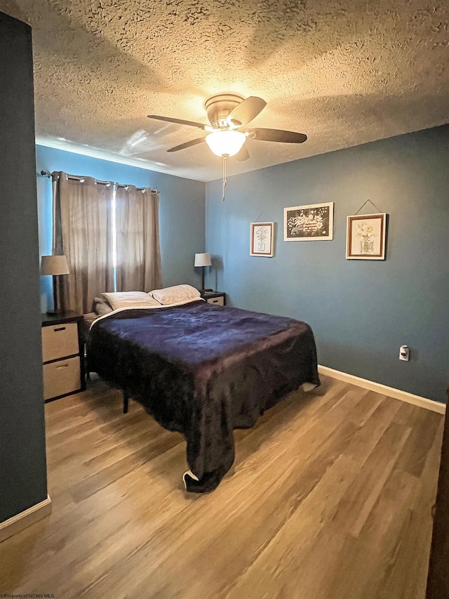 bedroom featuring a textured ceiling, baseboards, wood finished floors, ceiling fan, and pool table